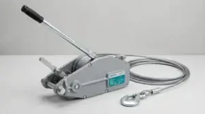 A heavy-duty manual wire rope hand winch with a steel cable and safety hook is displayed on a clean surface against a neutral background
